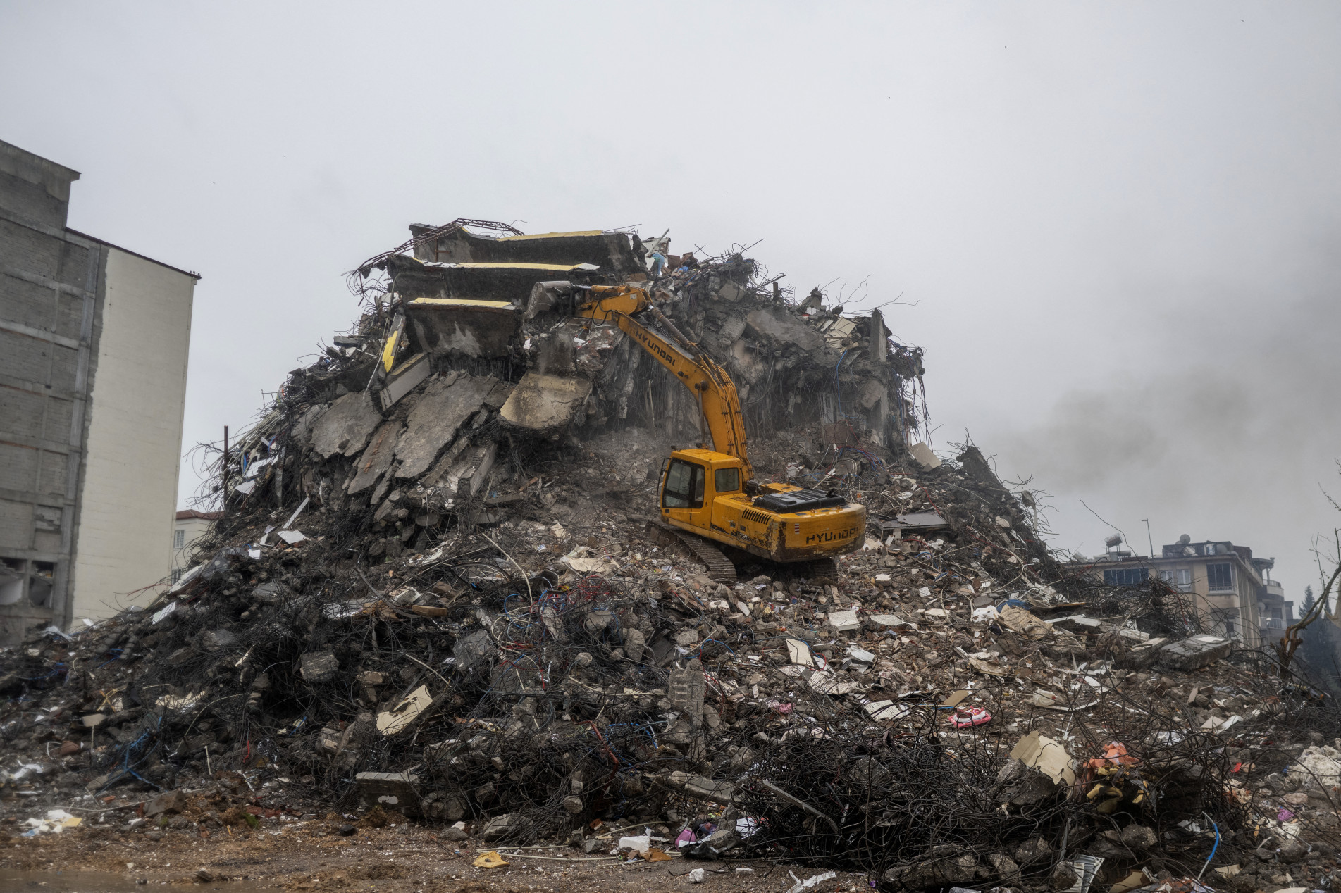  A digger stationed on a mound of rubble breaks down a destroyed building following a massive earthquake last month, in Adiyaman, southeastern Turkey on March 25, 2023. - On February 6, 2023, a 7.8-magnitude earthquake killed more than 50,000 in southeastern Turkey and nearly 6,000 over the border in Syria, leaving entire cities in ruins. Hundreds of thousands of Turkish quake survivors have been moved into tents and container homes across the disaster region, which covers 11 provinces across Turkey's southeast. (Photo by BULENT KILIC / AFP)
      Caption