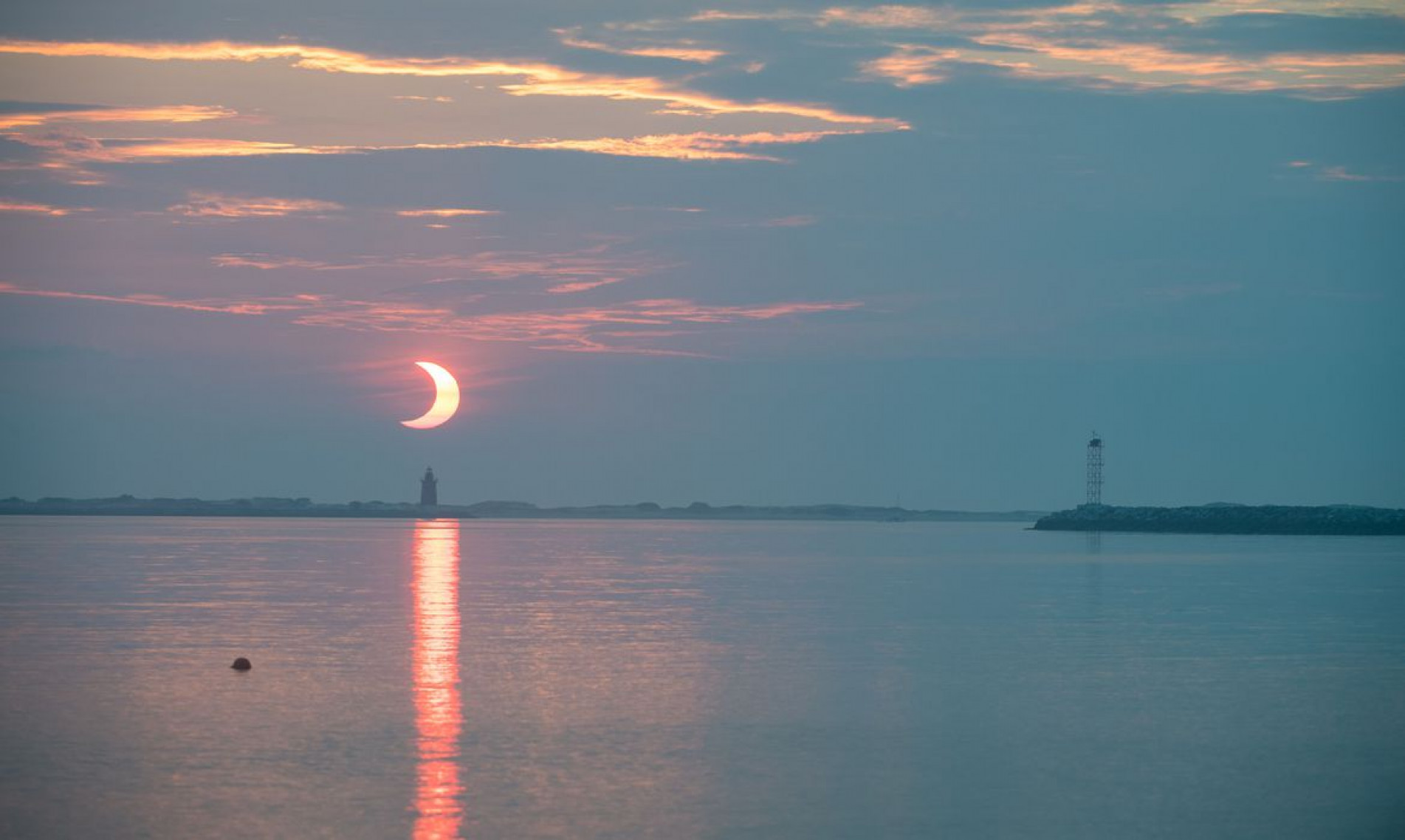 A partial solar eclipse is seen as the sun rises behind the Delaware Breakwater Lighthouse, Thursday, June 10, 2021, at Lewes Beach in Delaware. The annular or “ring of fire” solar eclipse is only visible to some parts of Greenland, Northern Russia, and Canada. Photo Credit: (NASA/Aubrey Gemignani)