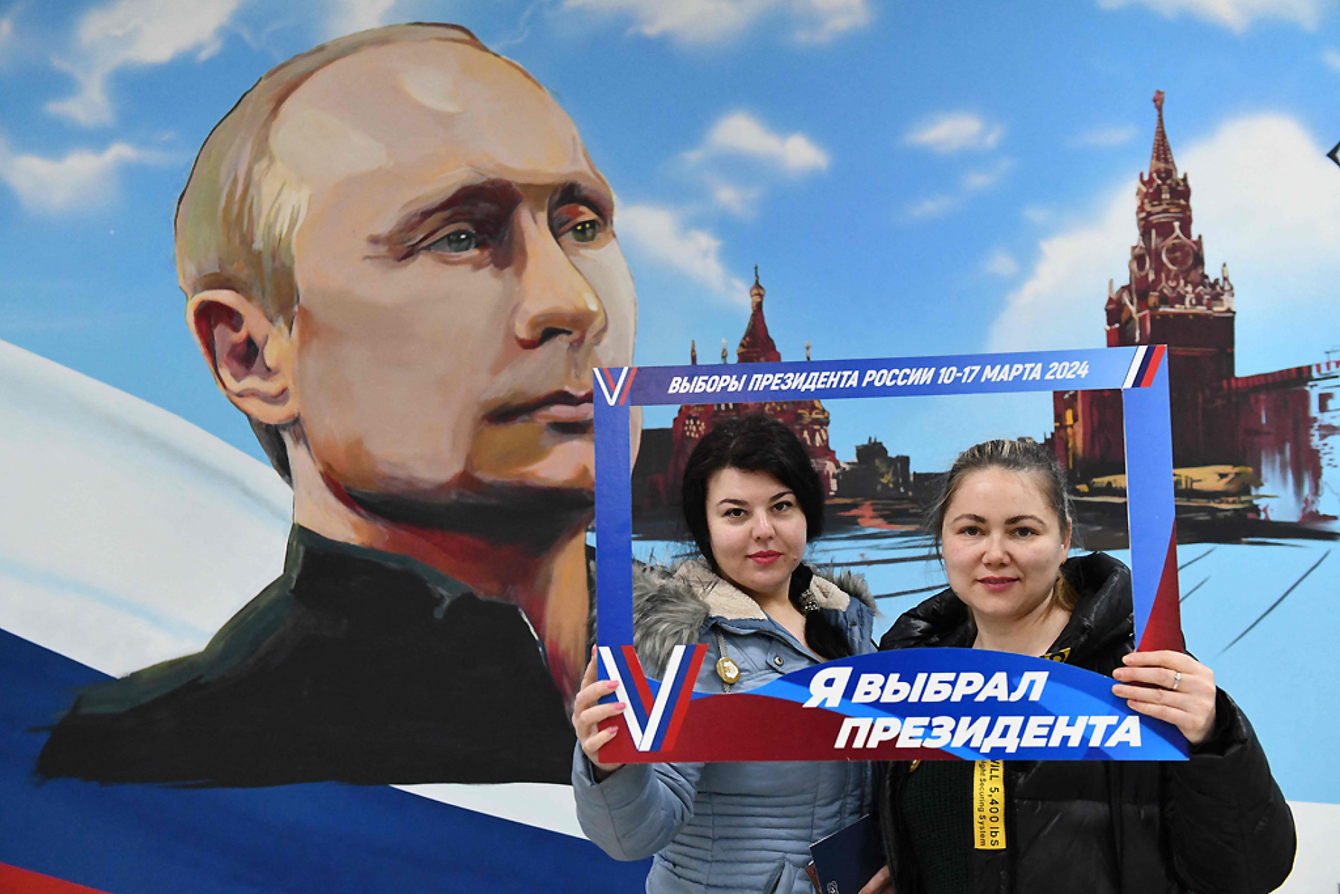 Mulheres posam em frente a um mural representando o presidente russo Vladimir Putin após votar nas eleições presidenciais da Rússia