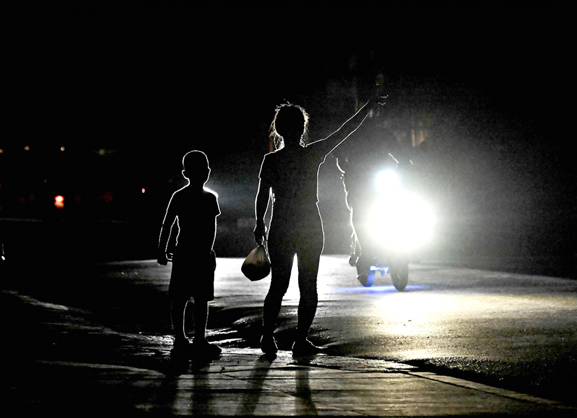 Uma mulher com seu filho sinaliza para um carro, em rua escura, durante apagão no município de Bauta, Cuba